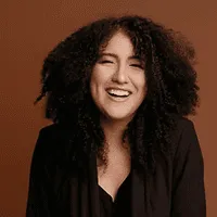 Laughing woman with voluminous dark curls in a black blazer.