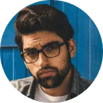 Portrait of a man with beard and glasses against a blue background.
