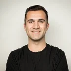 A person with short dark hair is smiling while wearing a black t-shirt.