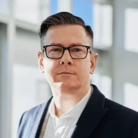 Professional portrait of a man with glasses and short dark hair wearing a blazer.